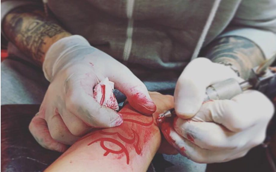 action shot of tattooing a red Balinese Om Symbol 